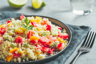 Couscous salad with fresh red and yellow bell peppers, avocado, tomatoes and lime. The concept of vegetarian and healthy food.